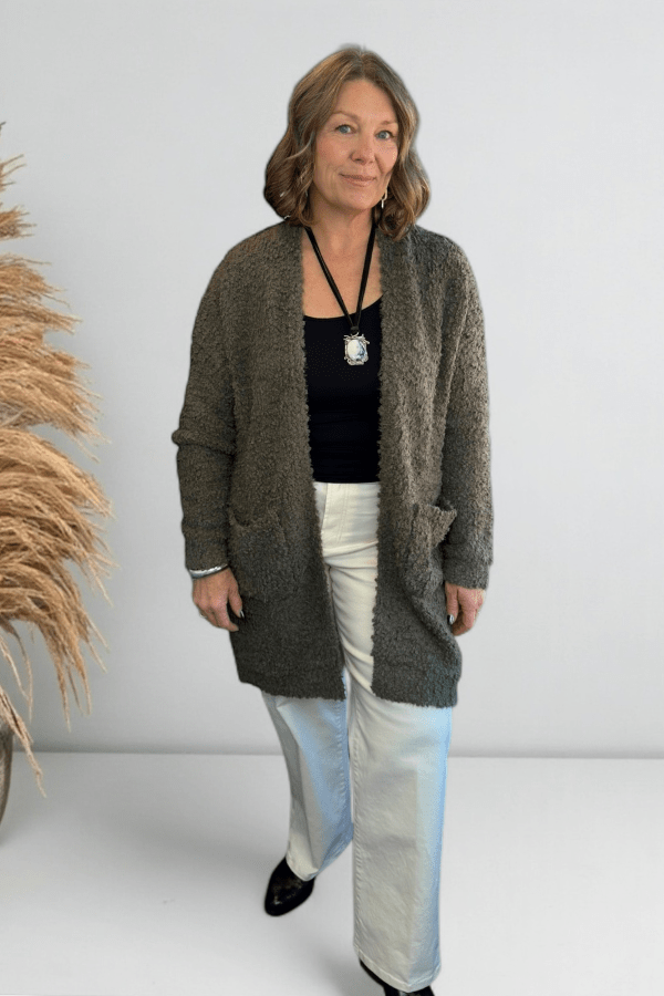 Model wearing an olive longline cardigan layered over a neutral top and denim.