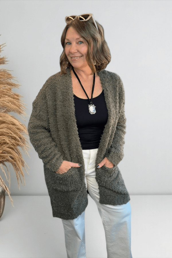 Model wearing an olive longline cardigan layered over a neutral top and denim with a statement necklace.