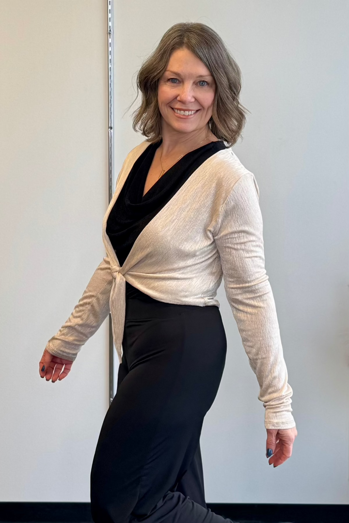 Woman smiling wearing a gold cardigan over a black top.