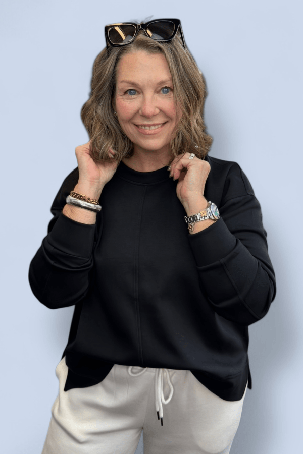 Woman wearing a black sweatshirt and white pants against a light blue background