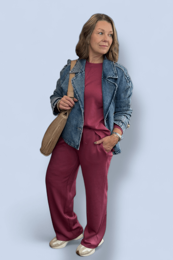 Woman wearing a denim jacket and maroon outfit with a beige bag on a light blue background