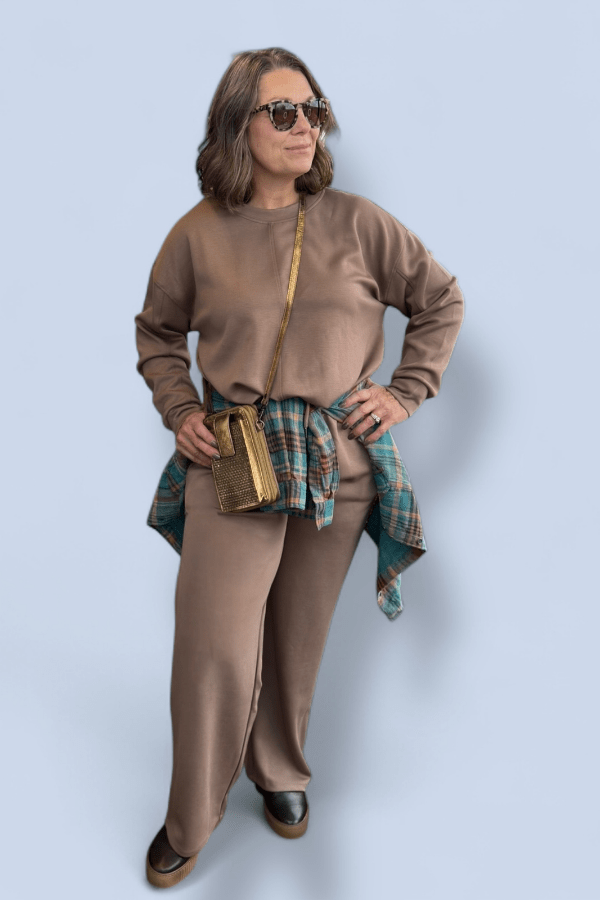 Woman wearing a brown outfit with sunglasses against a light blue background