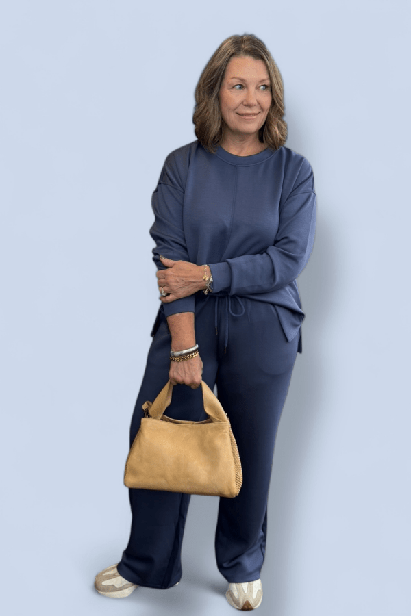 Woman in blue outfit holding a beige handbag against a light blue background