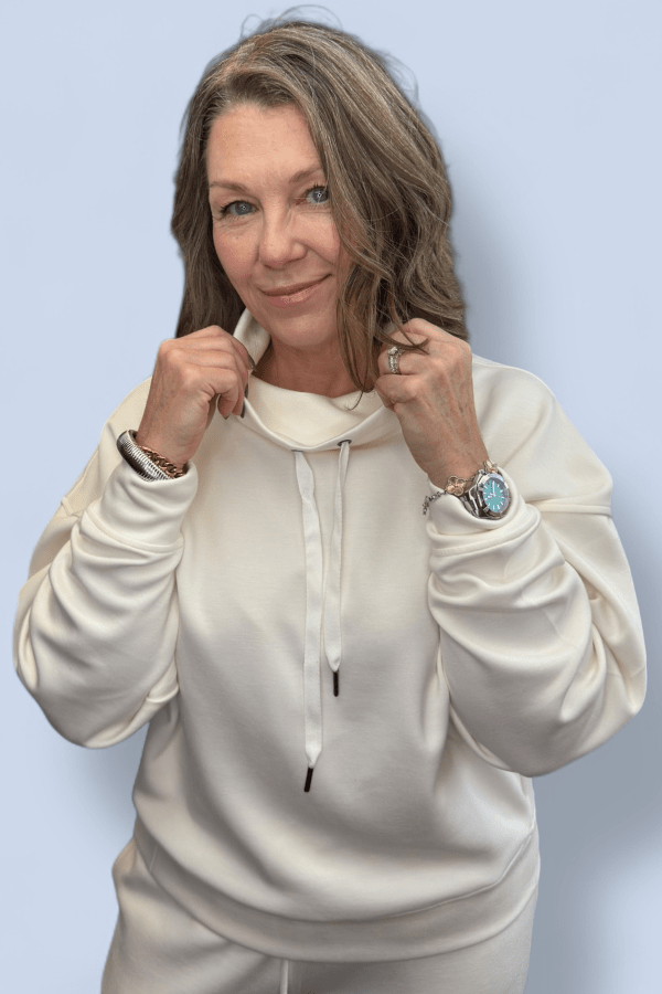 Woman wearing a cowl neck ivory sweatshirt against a light blue background.