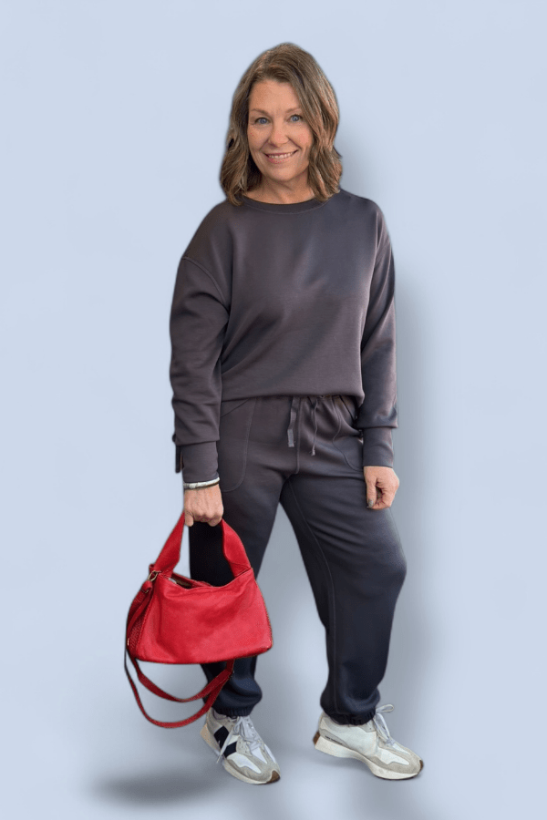 Woman in gray outfit holding a red bag against a light blue background