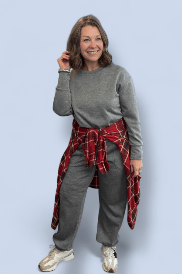 Woman wearing a gray outfit with a red plaid shirt over her shoulder against a light blue background