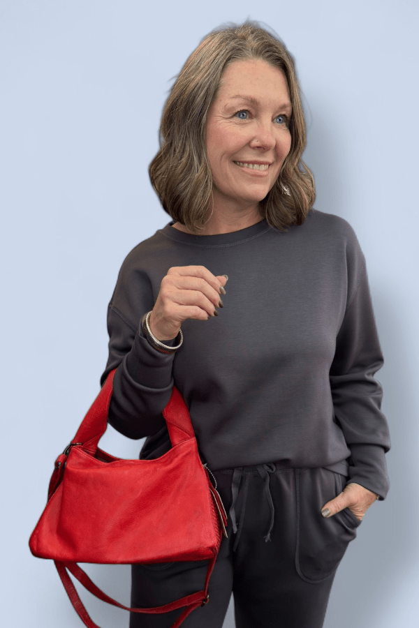 Woman wearing a dark gray set with a red purse on her arm.