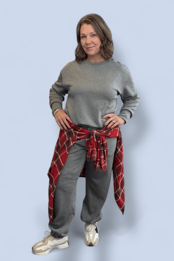 Woman wearing a gray outfit with red plaid top around her waist.