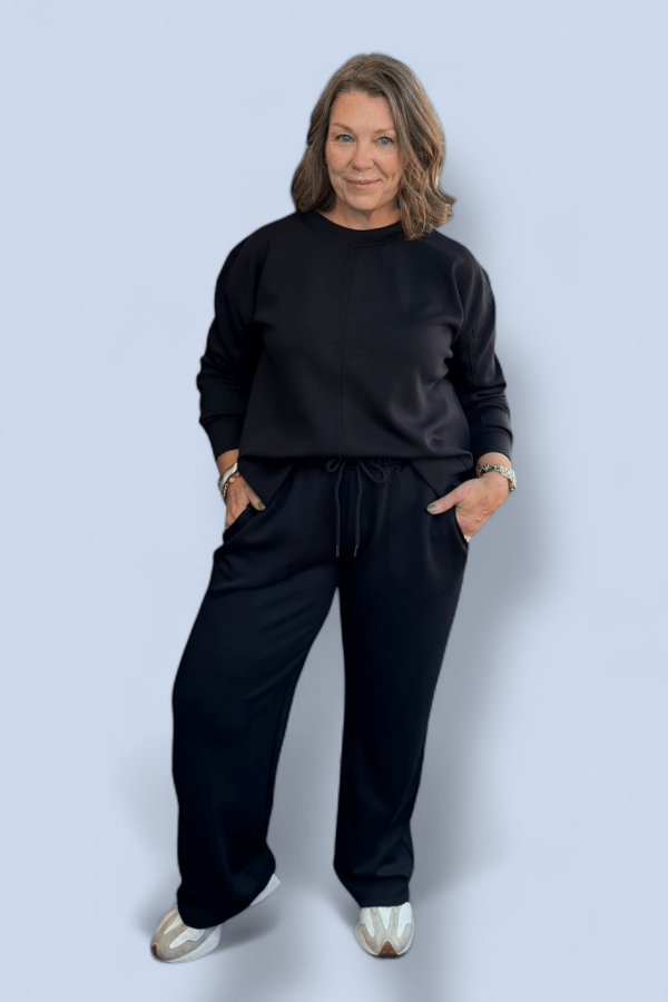 Woman wearing a black outfit with silver shoes on a light gray background