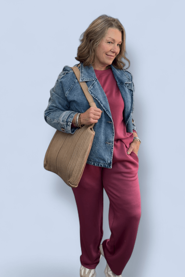 Woman wearing a denim jacket and pink pants holding a beige bag against a light blue background