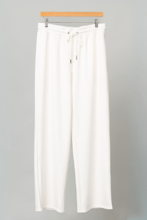 White pants on a wooden hanger against a gray background
