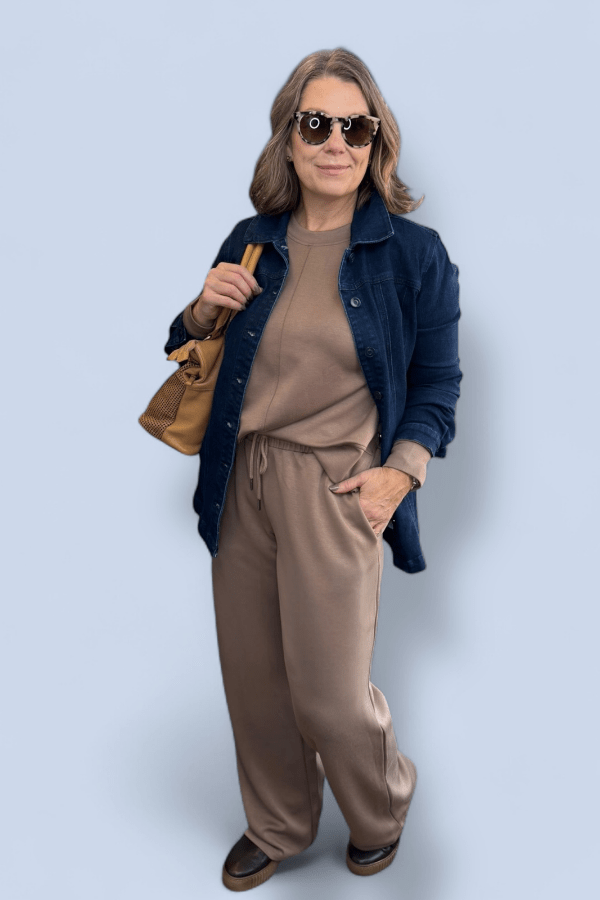 Woman wearing a navy jacket, brown top, and pants against a light blue background