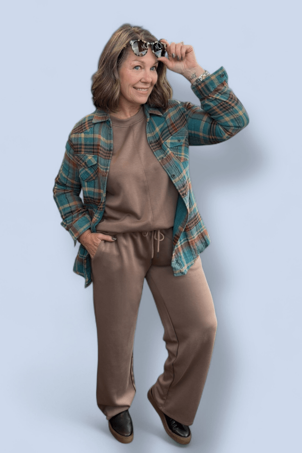Woman wearing a plaid shirt over a brown outfit against a light blue background