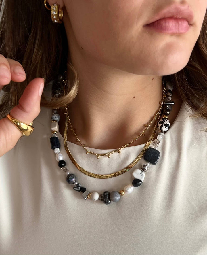 Close-up of a person wearing multiple necklaces with a neutral background