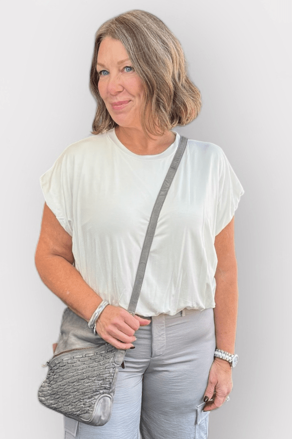 Woman wearing a white top and carrying a gray crossbody bag.