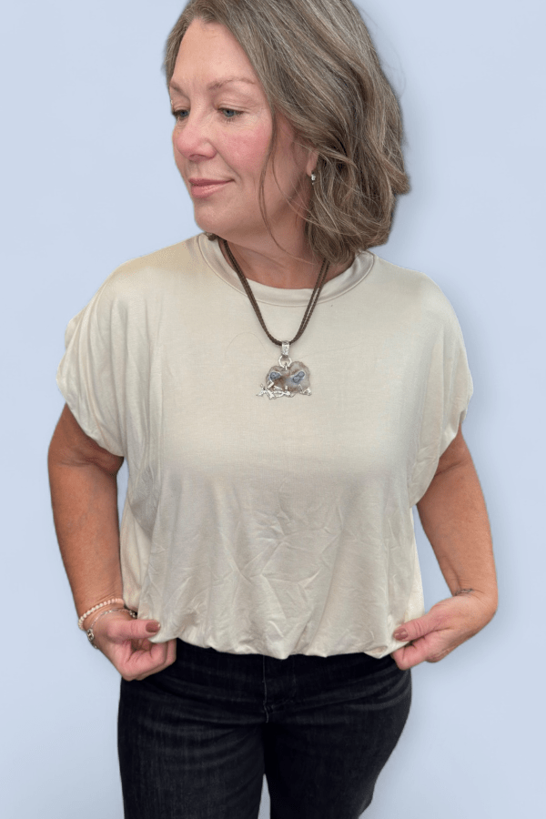 Woman wearing a beige top and black pants against a light blue background