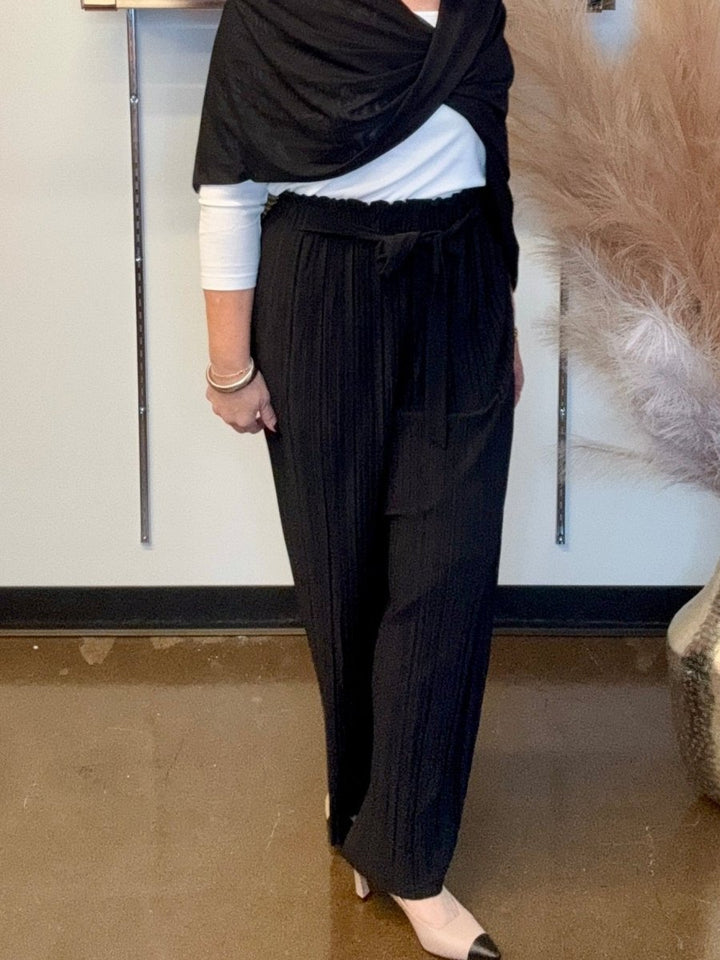 Tie Front Crepe Palazzo Pants in Black — front view showing high-rise paper bag waist with tie detail and pleated wide leg silhouette, styled with white top and black wrap

