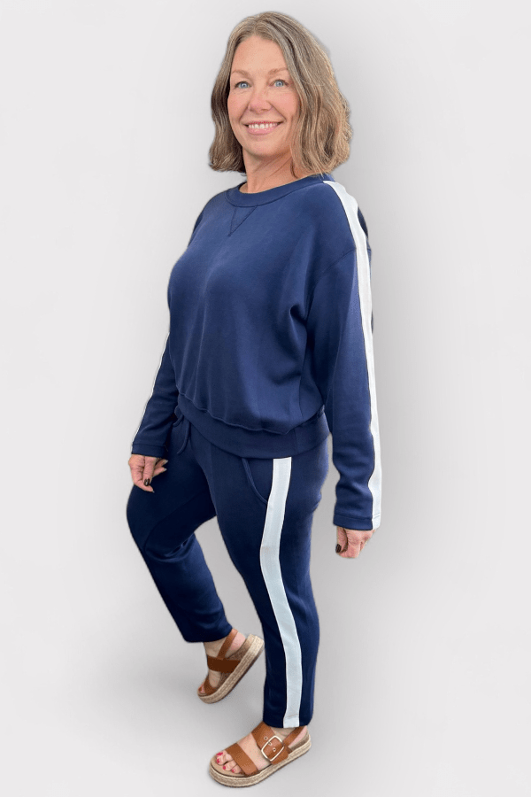 Woman wearing a navy tracksuit with white stripes on a plain background
