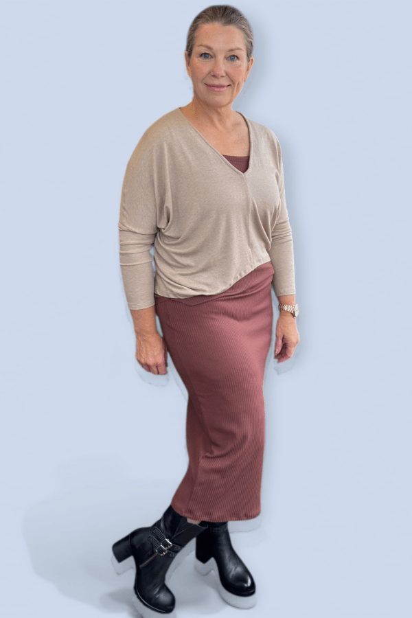 Woman wearing a brown midi skirt with boots and v neck tan top.