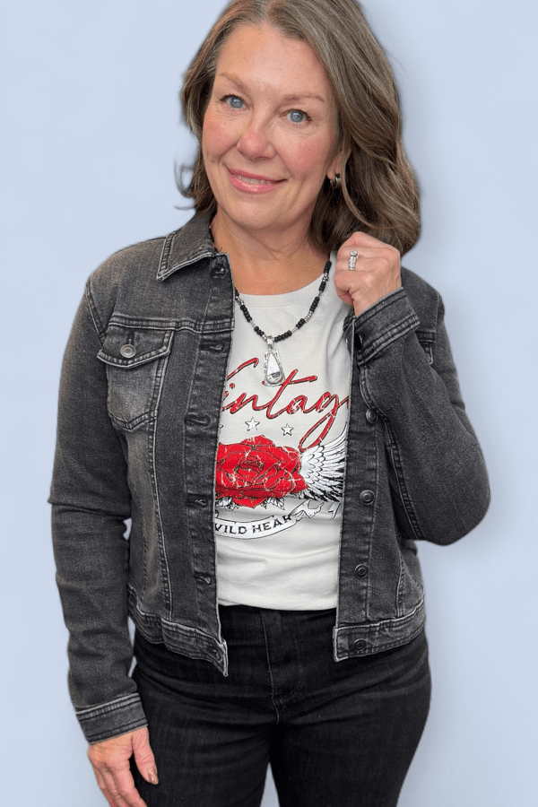 Woman wearing a denim jacket over a graphic t-shirt with a red rose design on a light blue background
