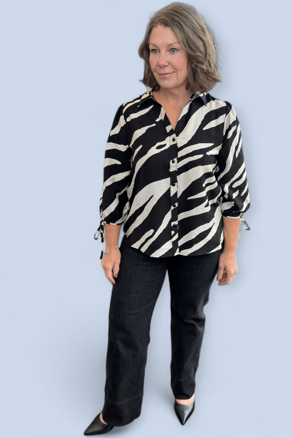 Woman wearing a zebra print shirt and black pants against a light blue background