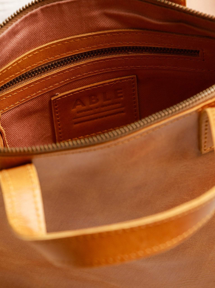 Close-up of ABLE Abera Convertible Backpack interior showing cotton lining, zipper pocket, and embossed leather brand patch
