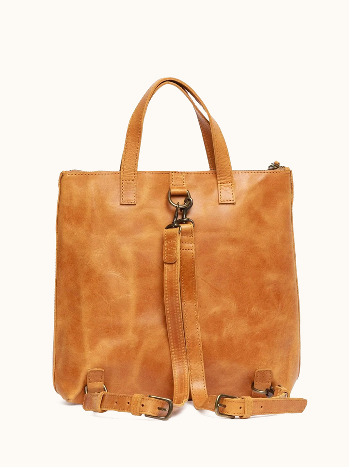 ABLE Abera Convertible Backpack in Cognac carried as a tote with dark wash denim and black slingback flats, front view on model