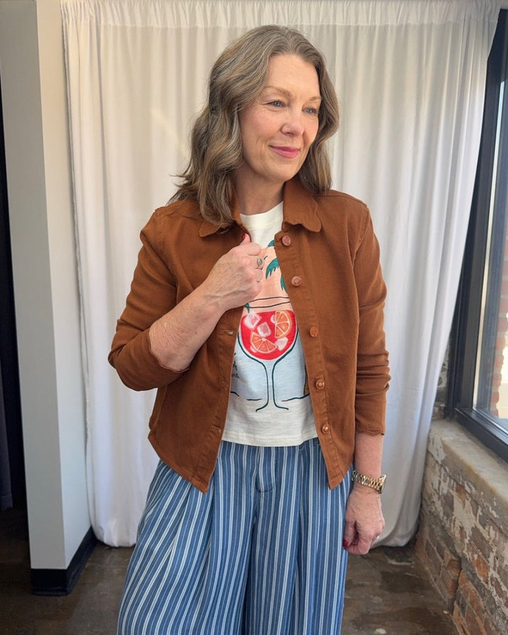 Wildfox Aperol State of Mind Nova Tee in Snow White under scalloped rust color denim jacket with blue and white striped pants, model with hand on jacket lapel, front view
