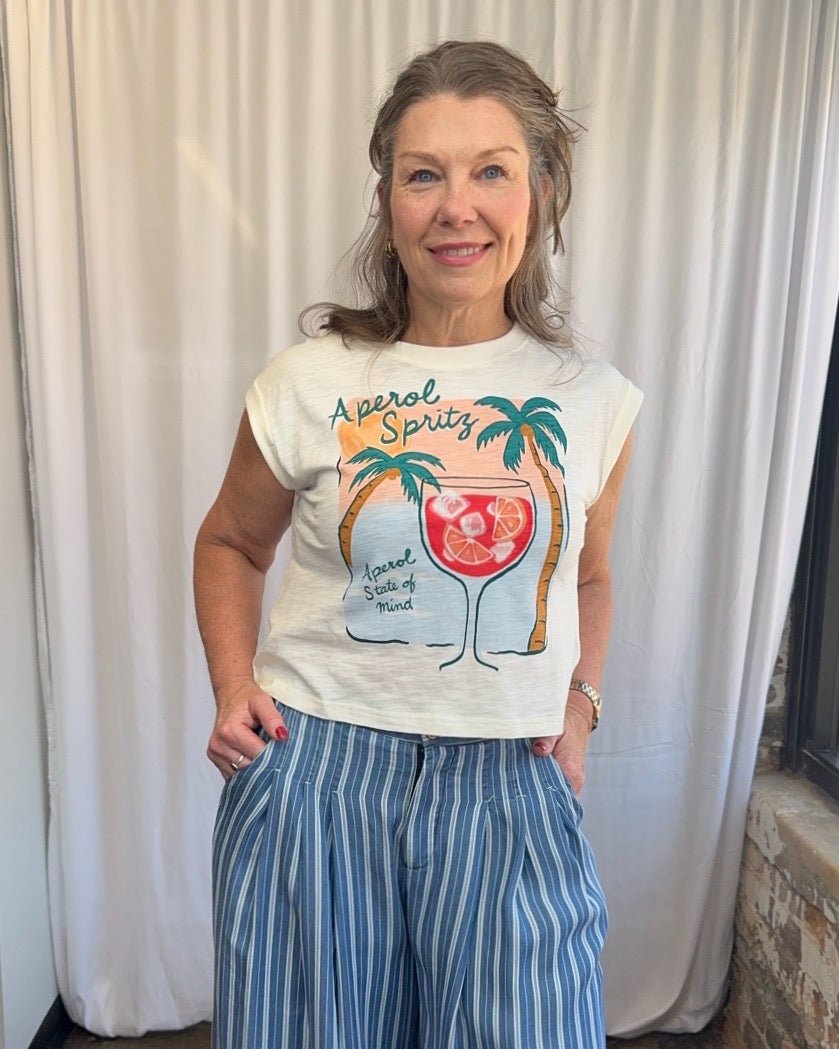 Woman wearing a t-shirt with a tropical design and text, standing against a white curtain.