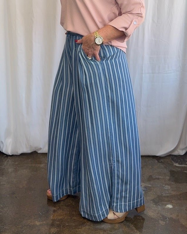 Blue and white stripe wide-leg pleated pants with single button waist and deep side pockets, full length side view on model styled with blush pink tunic and wood block heel sandals

