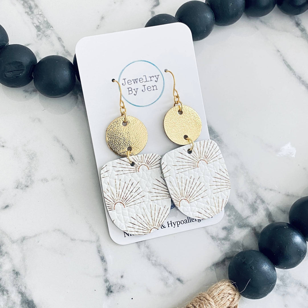 A pair of ivory and gold boho earrings with a sunburst. 