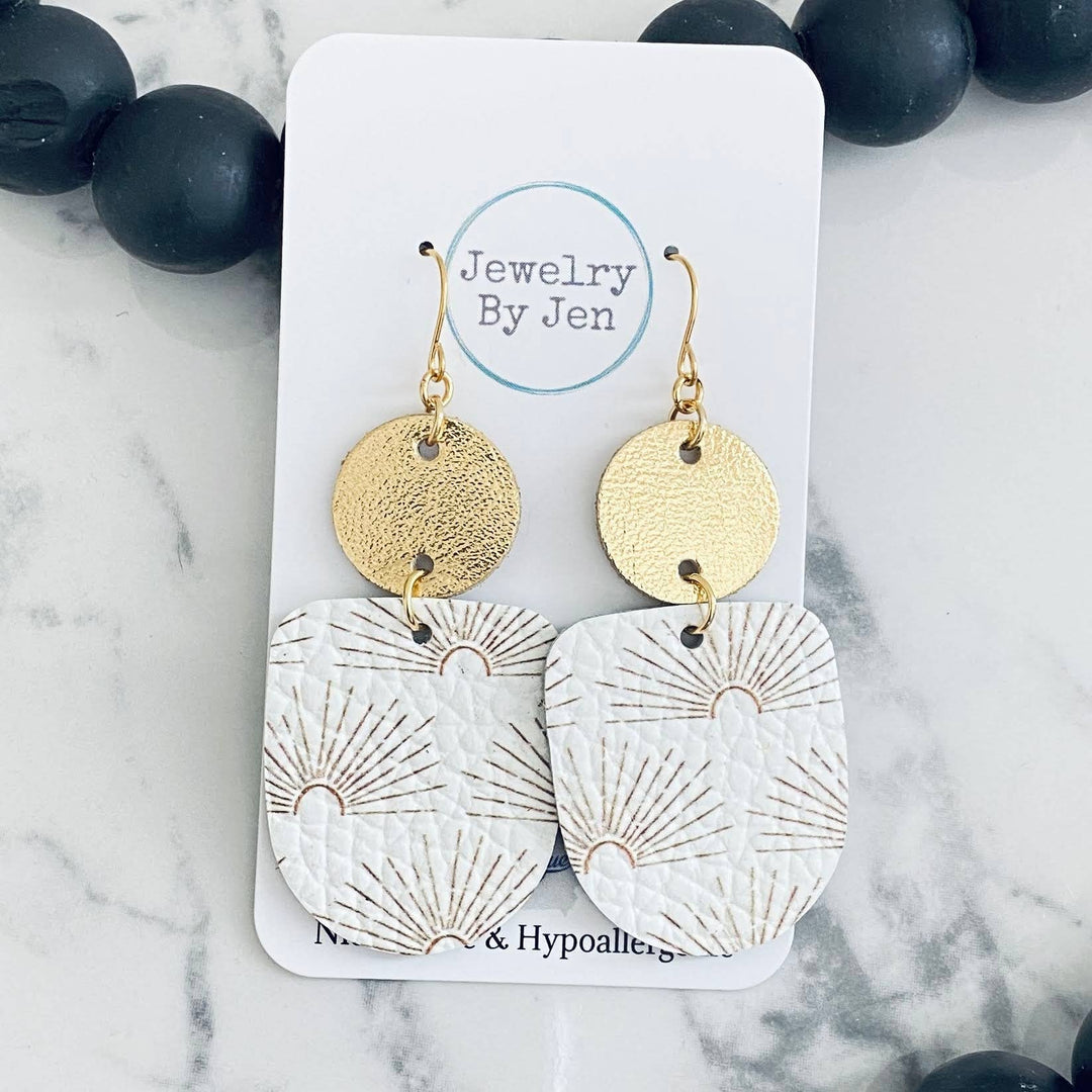 A pair of gold-colored earrings with a sunburst pattern on a white background, displayed on a card with &