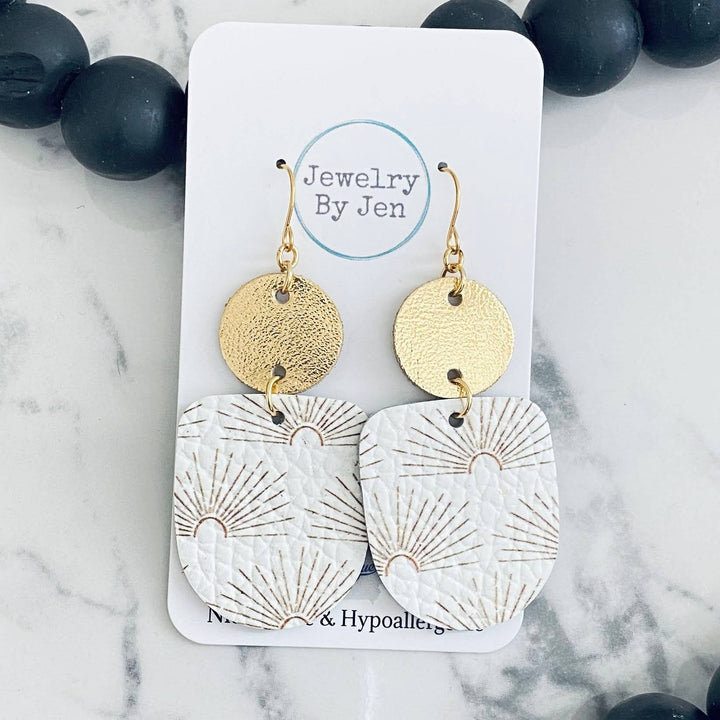 A pair of gold-colored earrings with a sunburst pattern on a white background, displayed on a card with &