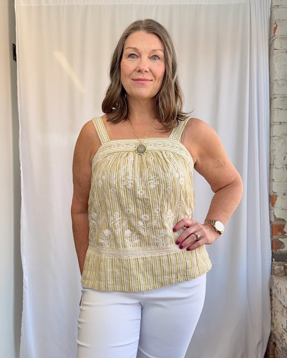 Woman wearing a yellow top with floral patterns against a white curtain background