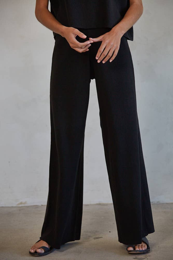 Woman wearing black ribbed pants shown from the waist down.
