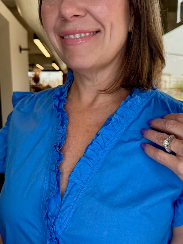 Close-up detail of the azure blue Ellie Sleeveless Ruffle Button-Up Top by Dear John Denim, highlighting the ruffled V-neckline, button-front placket, and crisp cotton poplin fabric.