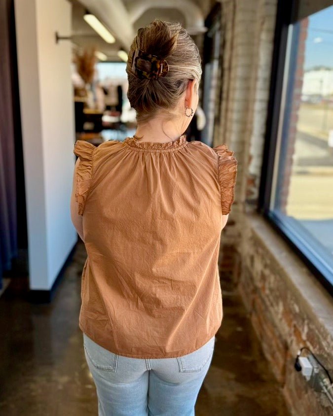 Our model is wearing a size Small in the biscuit Puja Top by Dear John Denim, shown from the back highlighting the smocked ruffle neckline and flutter sleeve detail, paired with light wash straight-leg denim.