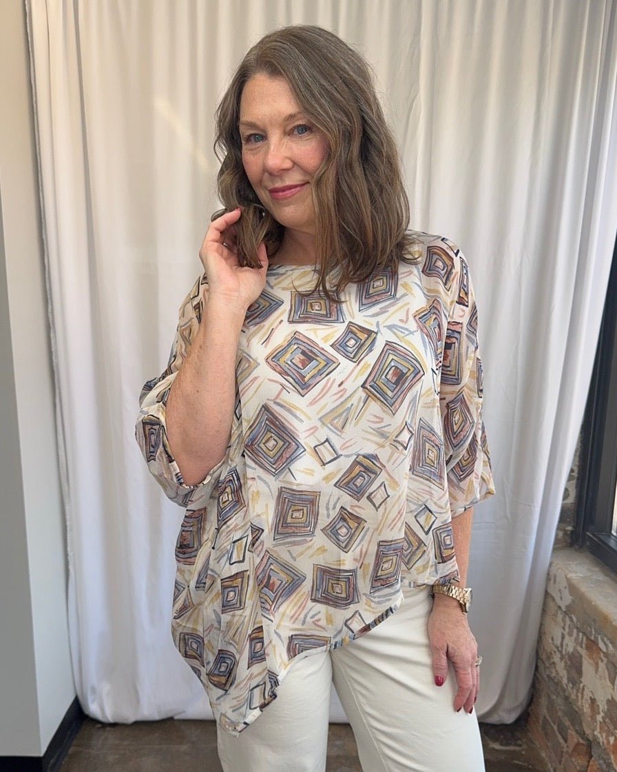 Lior Geometric Diamond Print Asymmetrical Blouse in cream, multicolor diamond print with asymmetrical hem, hand raised to collar, close-up front view on model
