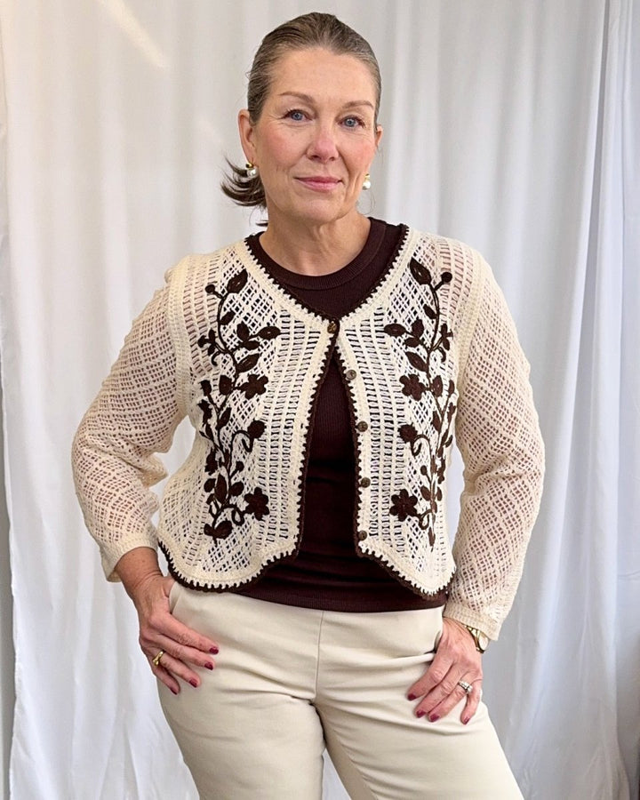 Woman wearing a beige lace cardigan over a brown top with a white background