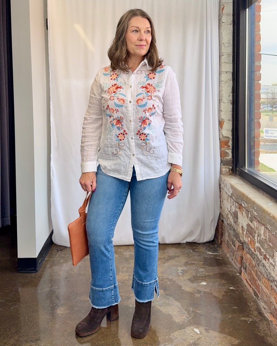Woman wearing an embroidered shirt and jeans standing indoors.