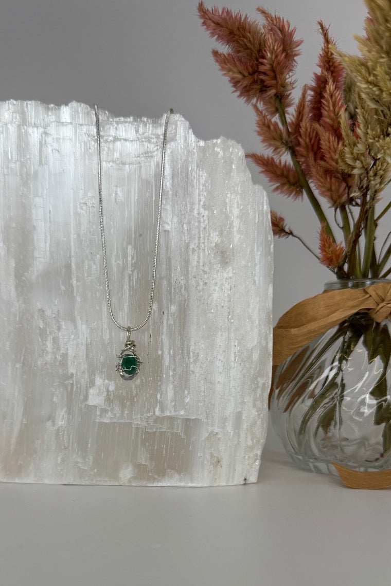 Raw Emerald Wire-Wrapped Pendant Necklace in Green & Silver — necklace displayed beside dried flowers