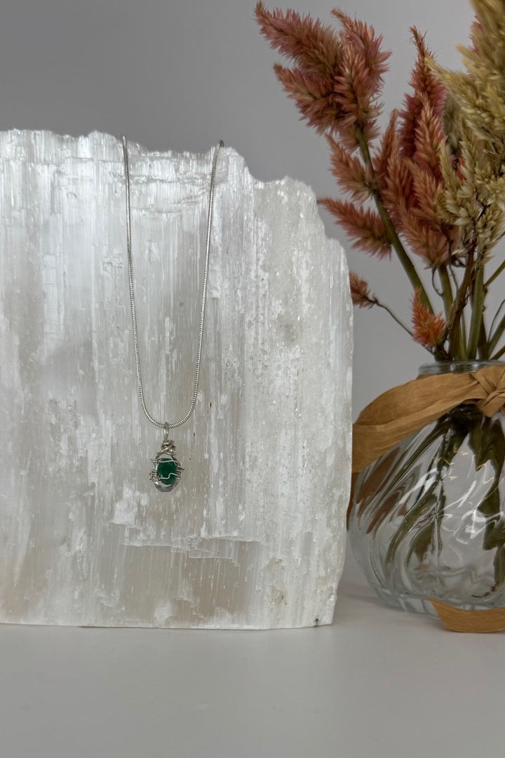 Raw Emerald Wire-Wrapped Pendant Necklace in Green &amp; Silver — necklace displayed beside dried flowers