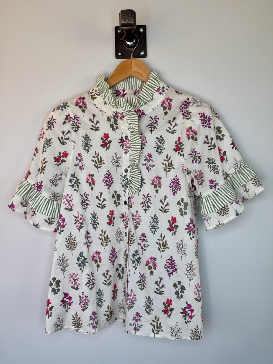Floral blouse with ruffled collar and sleeves on a hanger against a plain background