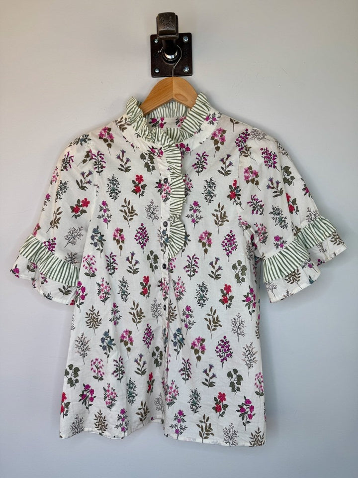 Floral blouse with ruffled collar and sleeves on a hanger against a plain background