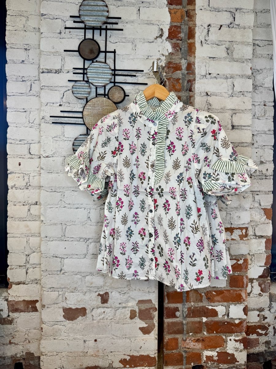 Entro floral and striped ruffle top hanging in a boutique setting with a white brick and industrial background.