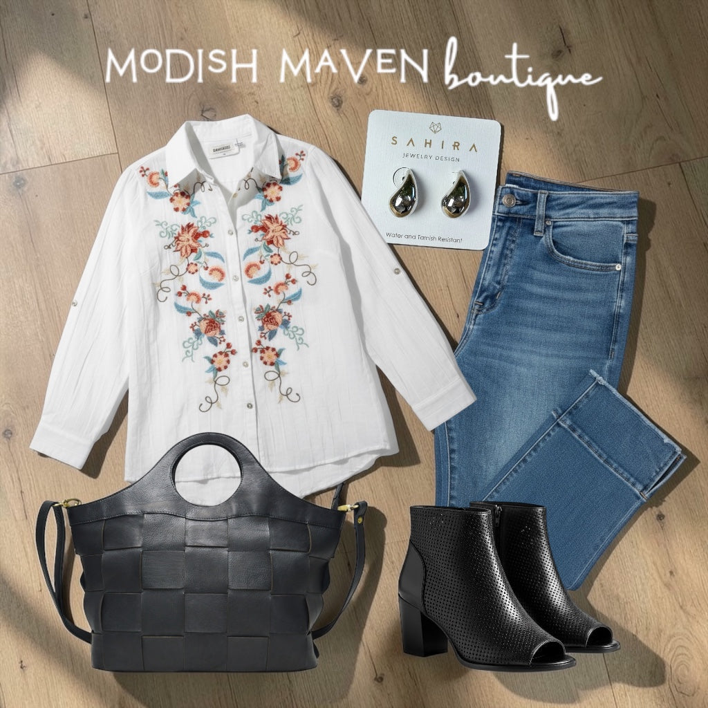 Fashion items including a white embroidered shirt, blue jeans, black boots, and a woven handbag on a wooden surface with 'Modish Maven Boutique' branding.