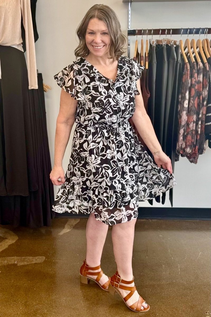 Marissa Olivia Floral Chiffon Ruffle Dress in Black/White floral, flutter sleeves and A-line ruffle hem styled with tan block-heel sandals, full outfit view on model