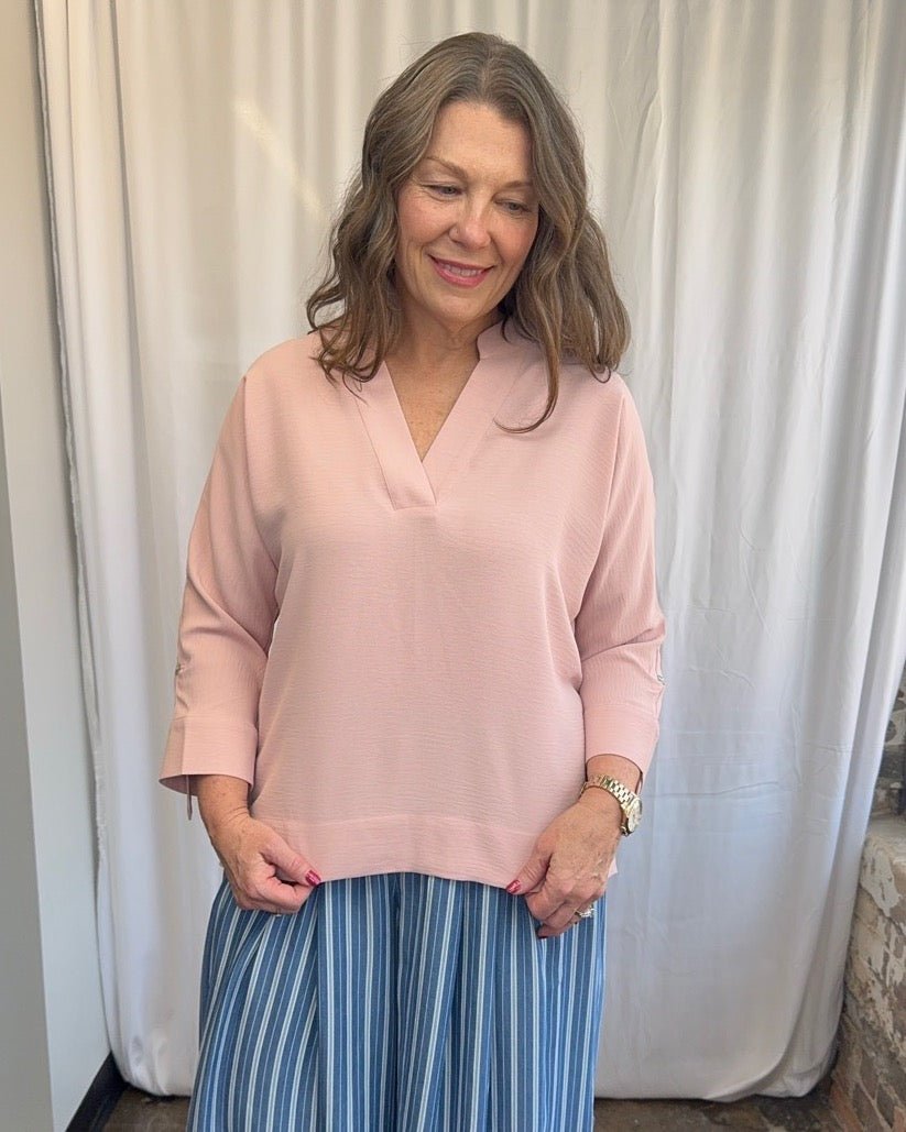 Frida Crossover V-Neck Tunic Blouse in blush pink with open V-neckline and 3/4 sleeves, styled with blue and white stripe wide-leg trousers, smiling full length front view on model
