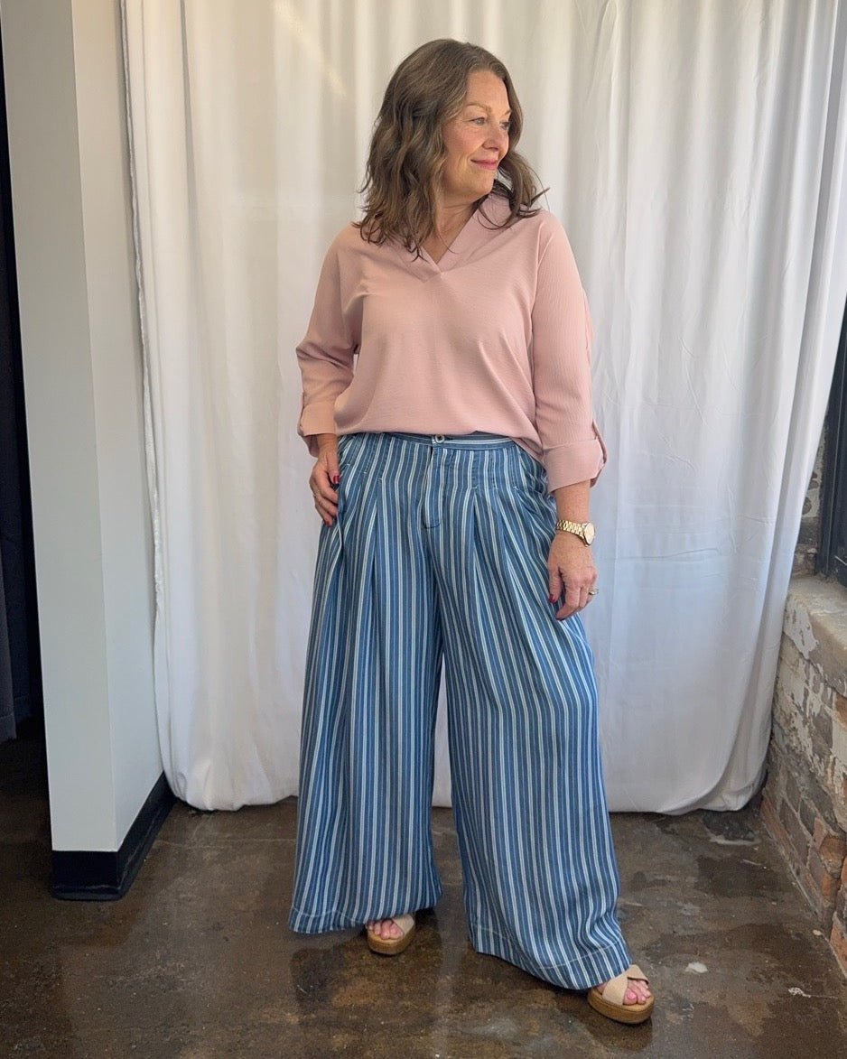 Frida Crossover V-Neck Tunic Blouse in blush pink with crossover V-neckline, styled with blue stripe wide-leg trousers and wood block heel sandals, full length front view on model
