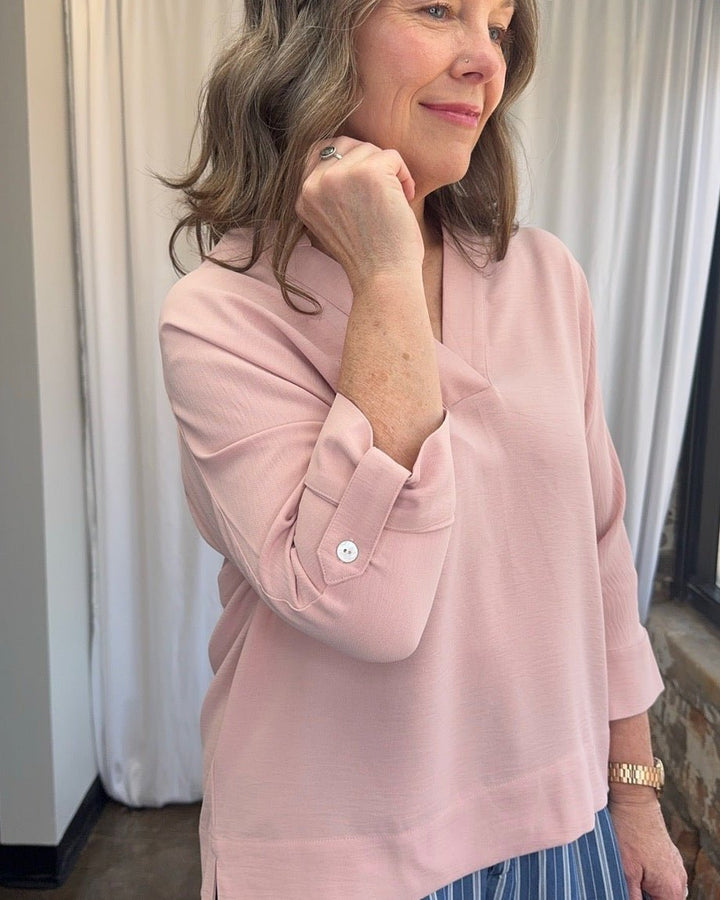Close-up of Frida Crossover V-Neck Tunic Blouse in blush pink showing button cuff detail on 3/4 sleeve, open V-neckline, and relaxed side split hem
